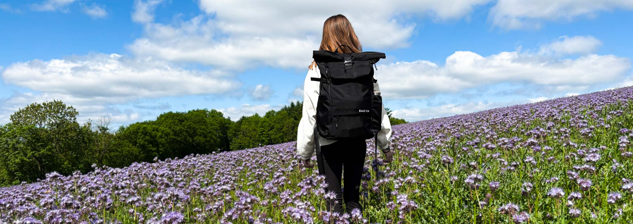 Mädchen mit schwarzem BALÔ-one-Rucksack läuft über eine lila-Blumenwiese.