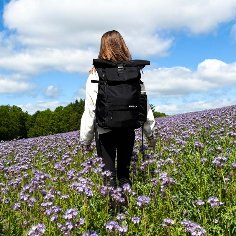 Mädchen mit schwarzem BALÔ-one Rucksack läuft über eine Blumenwiese.