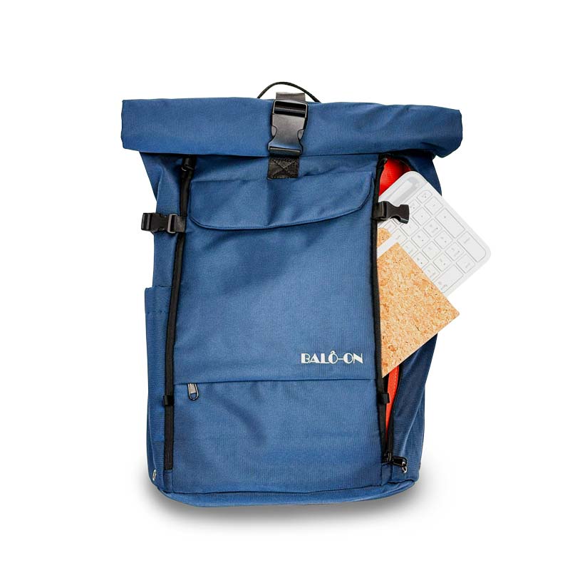 Blauer Rolltoprucksack der Marke BALÔ-ON, Vorderansicht, stehend auf weißem Hintergrund; schneller Zugriff auf das Hauptfach durch Reißverschluss, im Hauptfach sind eine Tastatur und ein Notizbuch zu sehen: