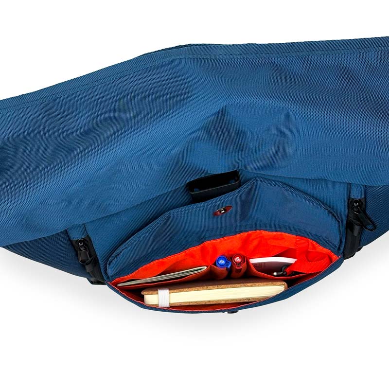 Blauer Rolltoprucksack der Marke BALÔ-ON, Ansicht von oben; geöffnete Fronttasche mit Magnetverschluss und Schlüsselanhänger, gefüllt mit Stiften und Notizbuch.