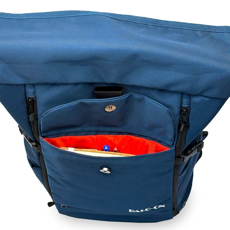 Blauer Rolltoprucksack der Marke BALÔ-ON, Ansicht von vorne, oben; geöffnete Fronttasche mit Magnetverschluss und Schlüsselanhänger, gefüllt mit Stiften und Notizbuch.