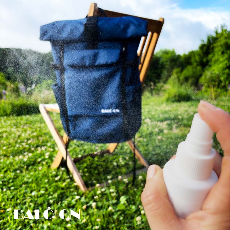 BALÔ-one blue Rucksack hängt an einem Gartenstuhl und wird gerade imprägniert; eine Hand sprüht Imprägnierspray auf das Material.