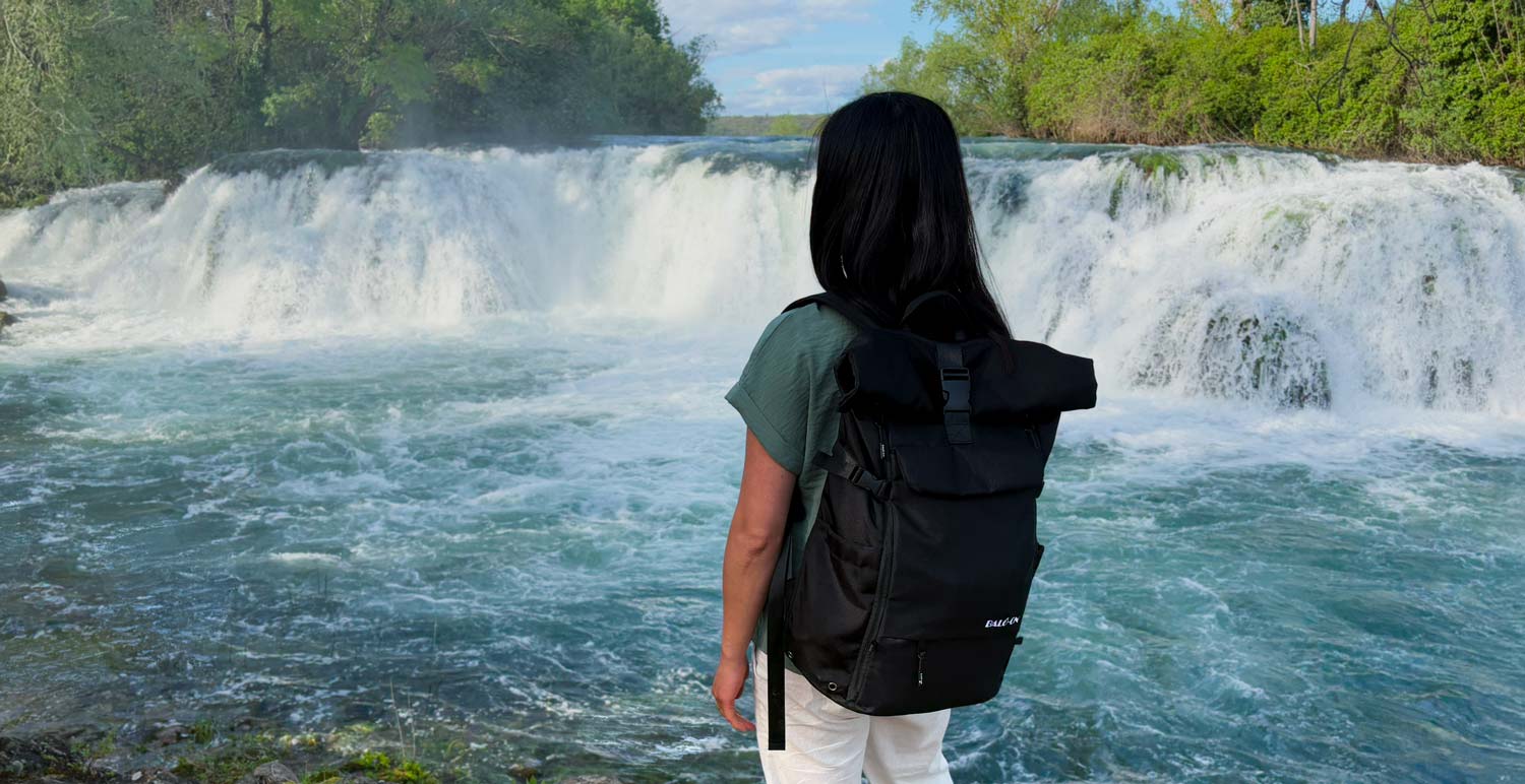 Junge Frau trägt BALÔ-one Black 25 Liter und steht an einem Wasserfall.