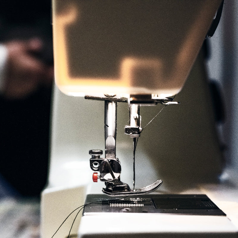 Nähmaschine mit eingefädelter Nadel, Nahaufnahme des Nähfußes und Fadens.